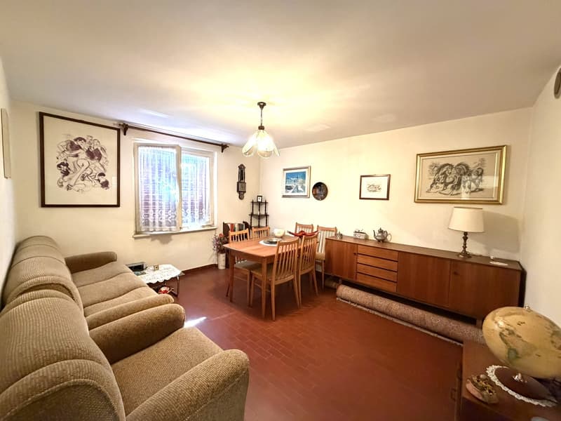 living room with couch, dining table, wooden floor, white walls, picture frames, lamp, cabinet, window with curtains