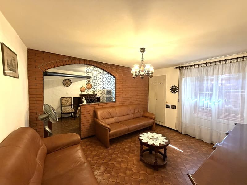 living room with two brown leather couches, brick wall, chandelier, coffee table, fan, mirror, window with white curtains