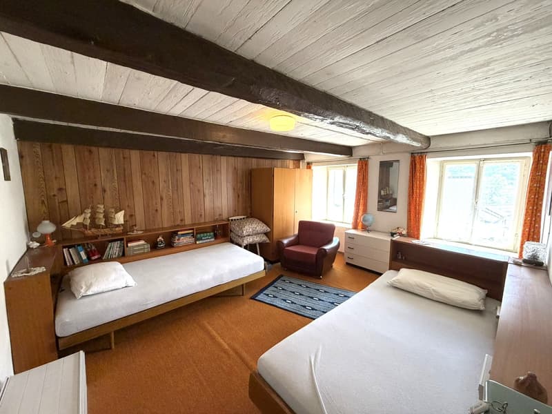 bedroom with two beds, wooden wall, wooden floor, wooden cabinet, chair, rug, windows with curtains