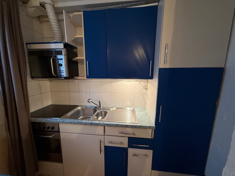 Stainless steel sink, electric stove, blue and white cabinets, microwave, tiled walls