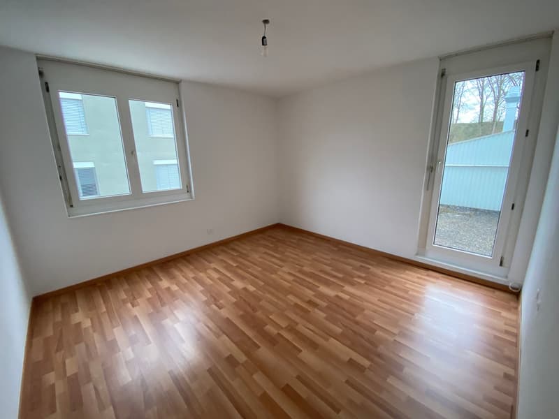 Empty room with wooden flooring, white walls, and large windows with blinds. No furniture or equipment present.