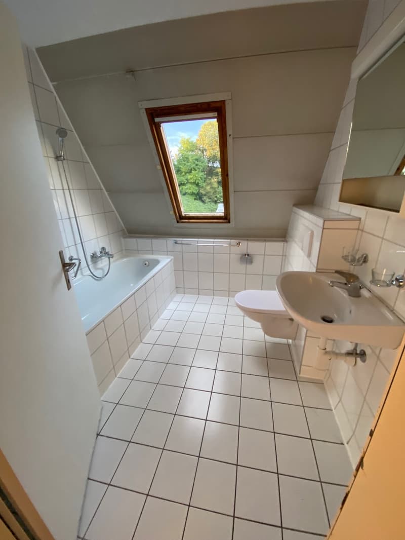 a small bathroom with white tiled floor, bathtub, toilet, sink, mirror, and a small window