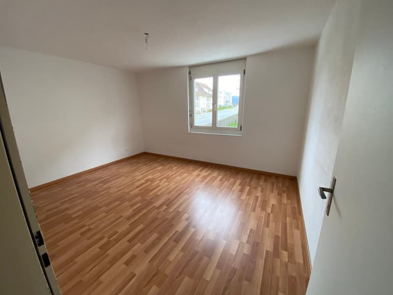 Empty room with wooden flooring and white walls, featuring a single window with a view of the street.
