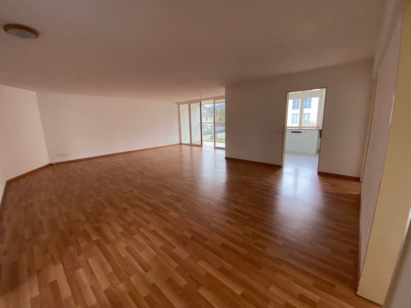 Empty room with wooden flooring, white walls, and large windows with sliding glass doors leading to an outdoor area.