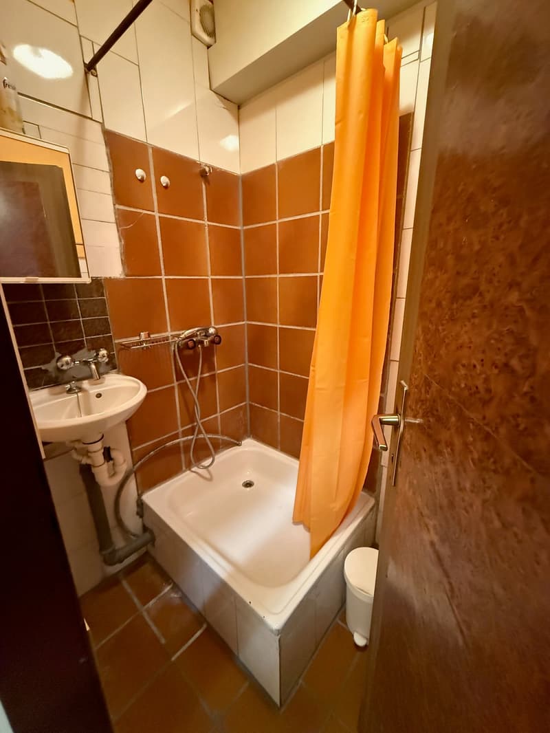 small shower area, square white shower tray, small sink, mirror, white tile walls, wooden door