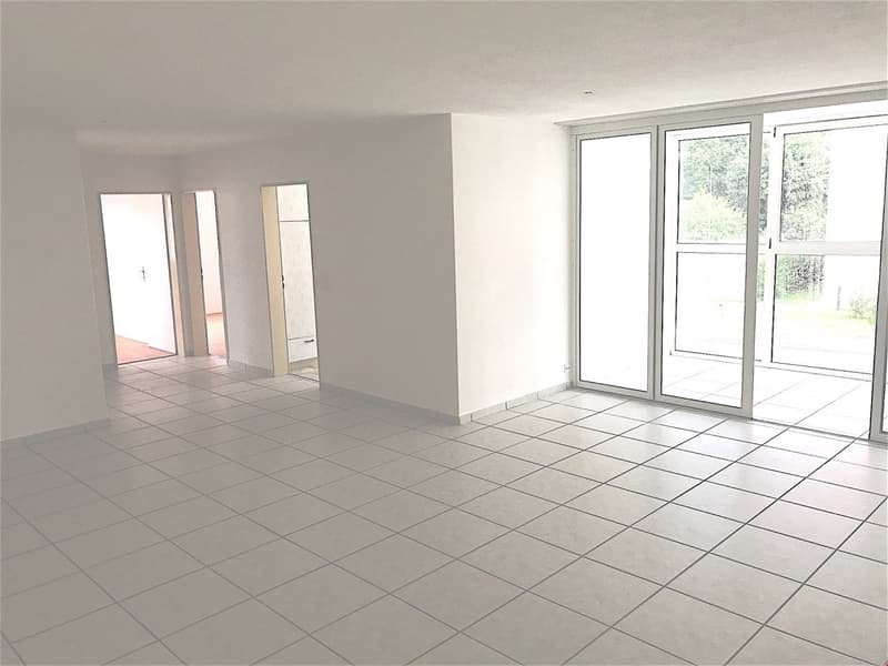 Empty room with white tiles, sliding glass doors, and a view of trees outside