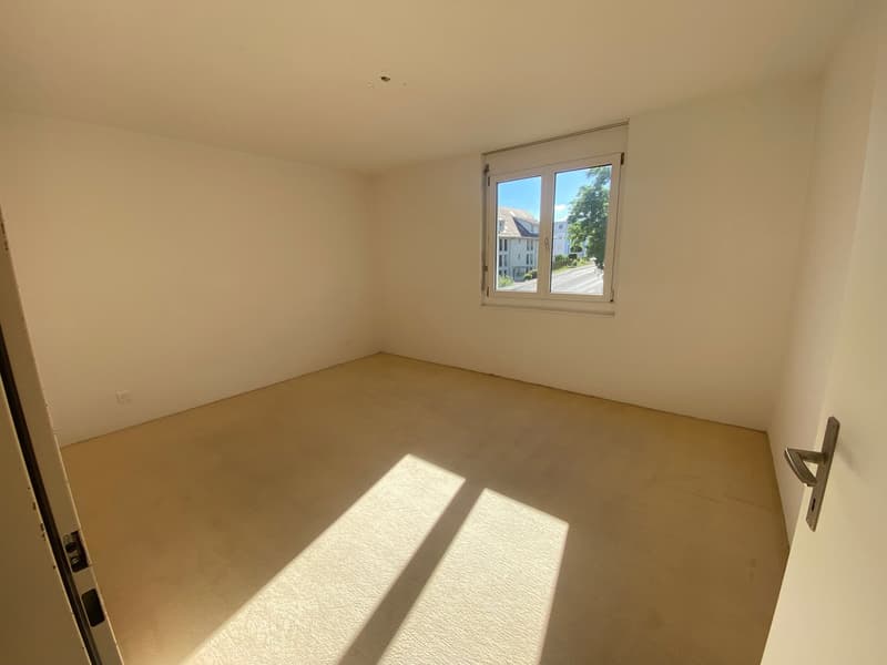 Empty room with white walls, light-colored carpet, and a single window letting in natural light.