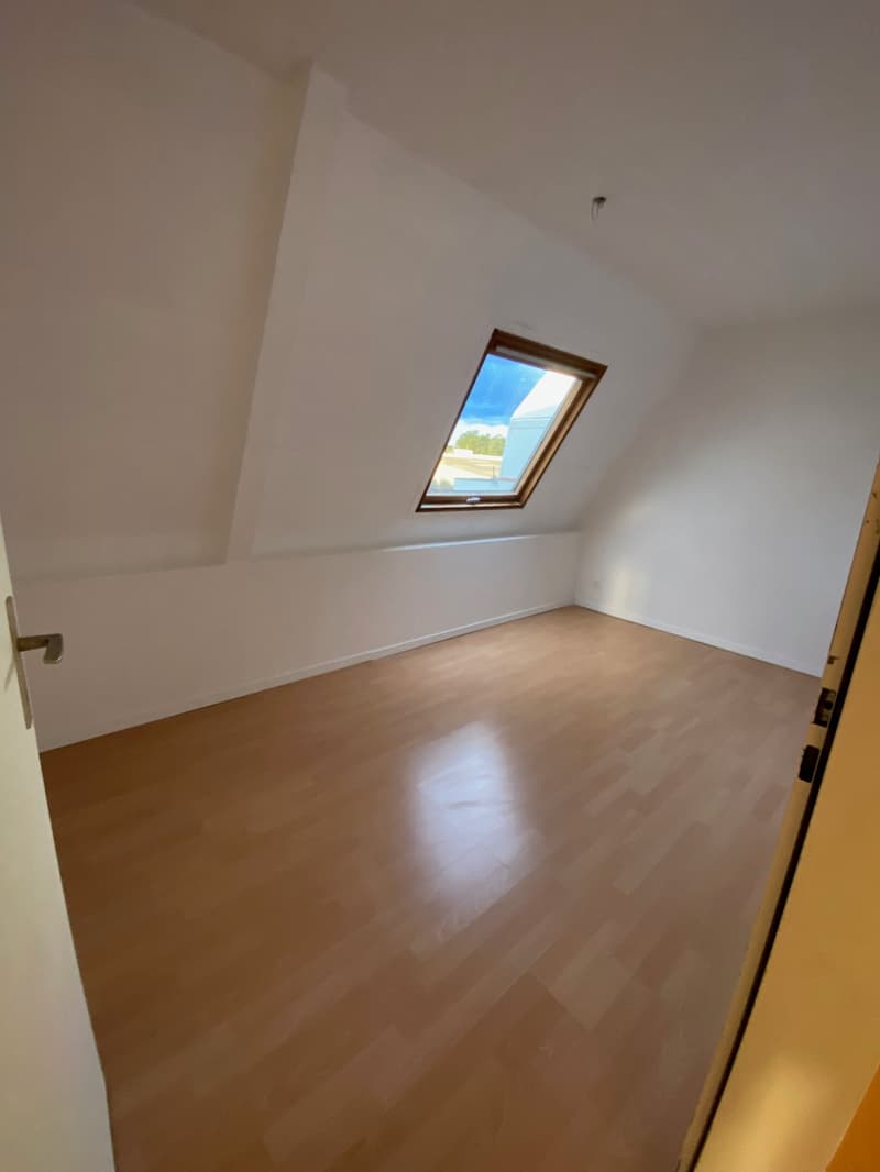 empty room with wooden floor, white walls, small window, slanted ceiling with skylight, open door