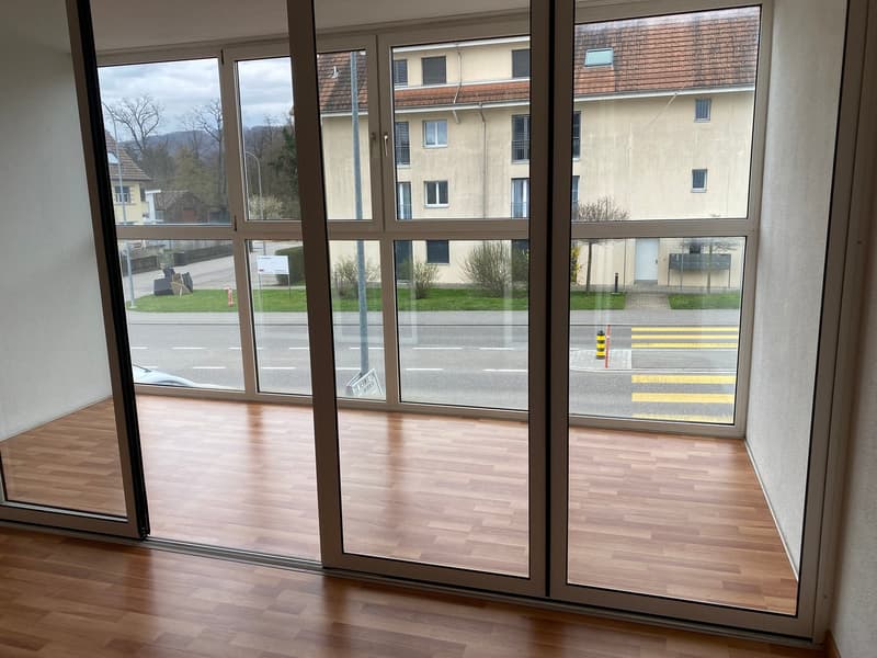 Empty room with wooden flooring and large glass sliding doors leading to a street view.