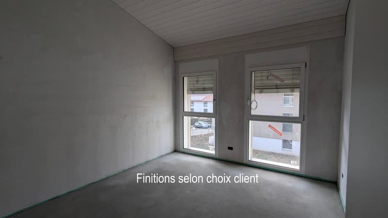 Empty room with bare walls and concrete floor, featuring two windows with blinds and a view of neighboring buildings.