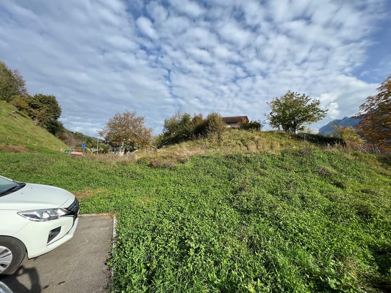 Empty lot with car parked on side, house on hill