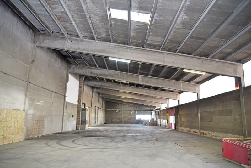Large open warehouse space with concrete floor, exposed ceiling beams, and concrete walls. The space appears to be empty and unfinished.