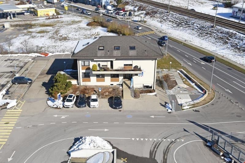 2-story commercial building with parking spaces in front, located near a road and railway tracks