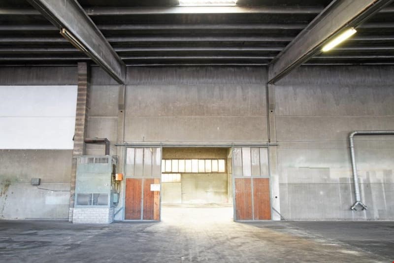 Large industrial warehouse space with concrete walls, metal beams, and open garage doors