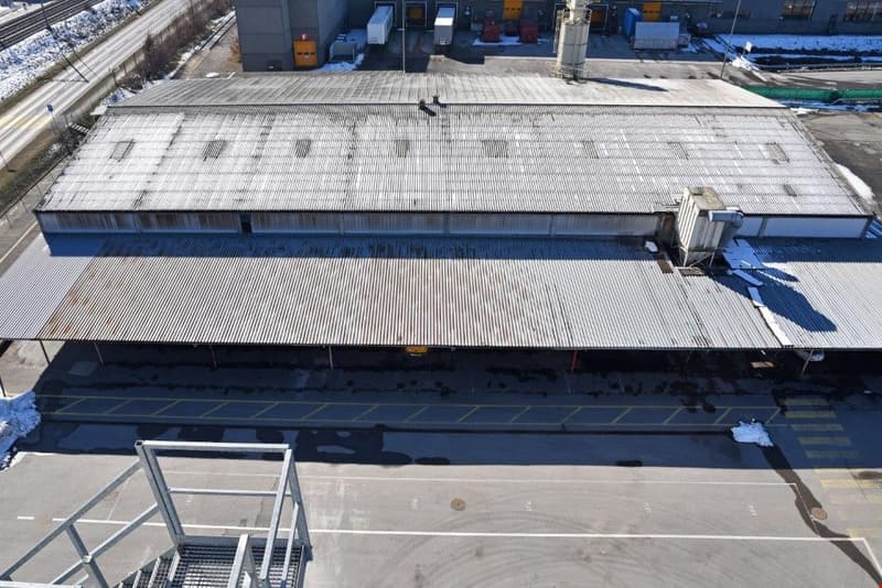 Large industrial warehouse or factory building with a metal roof and walls, surrounded by paved areas and other industrial structures.