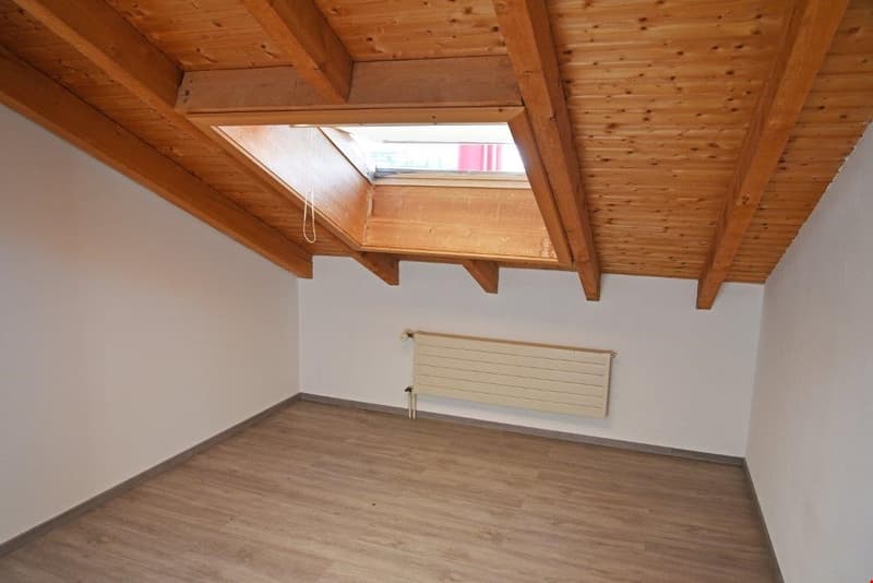 Attic bedroom with wooden ceiling beams, skylight window, and radiator heater