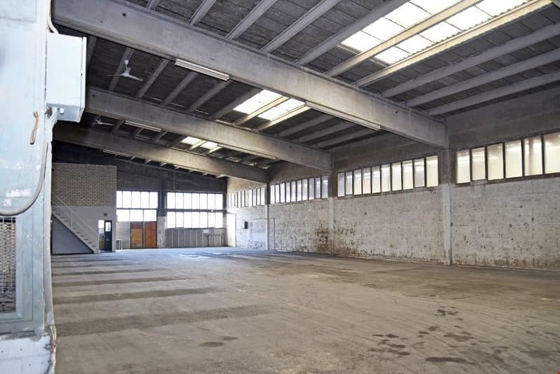 Large open space with concrete floor, exposed ceiling beams, and windows along the walls. The space appears to be a warehouse or industrial building.