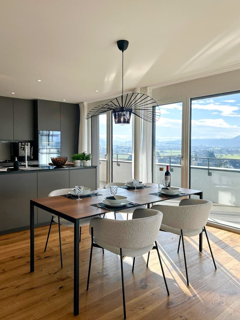 modern wooden dining table, white chairs, glass windows with view, hanging chandelier, grey kitchen background