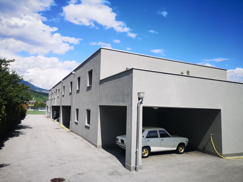 A multi-story commercial or industrial building with a garage entrance on the ground floor. The building has a modern, minimalist design with a gray exterior and large windows.