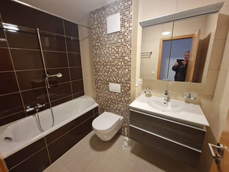 Bathroom with brown and white mosaic tile walls, bathtub, toilet, vanity with sink, and mirror