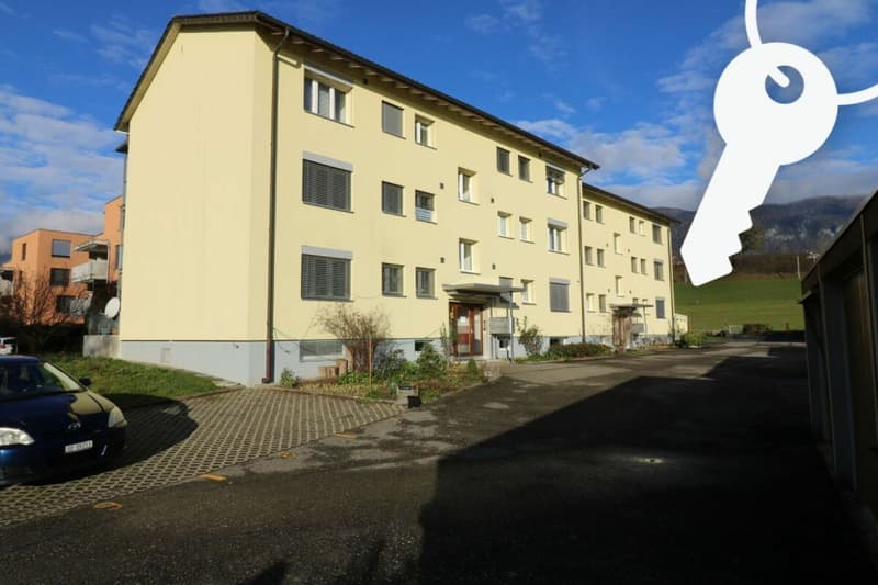 4 story apartment building, yellow exterior, parking lot in front, car parked