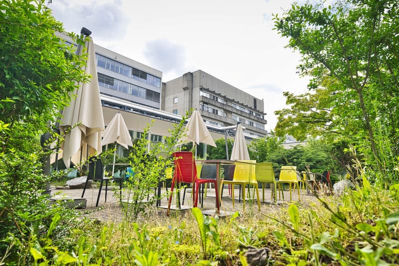 Outdoor dining area with tables and colorful chairs, closed umbrellas, and a building in the background.