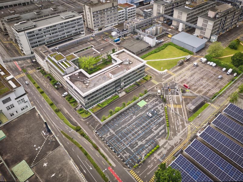 Industrial complex with multiple buildings, parking lot, solar panels, greenery, rooftop garden, wide roads, street lights
