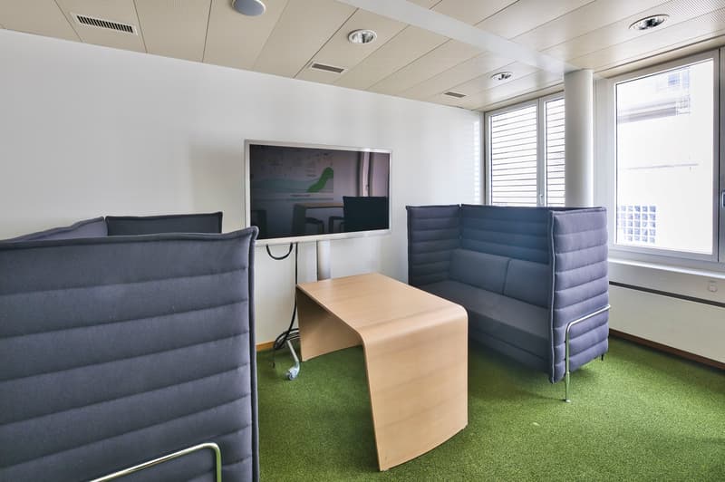 modern office room with blue couches, wooden desk, large windows, mounted television