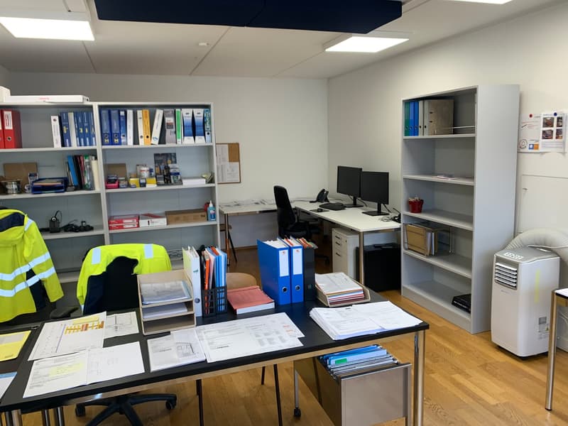 Two desks, bookshelves with many folders, computers, office equipment, wooden floor