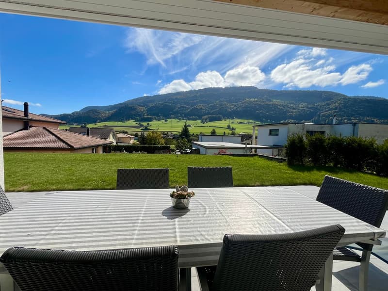 A balcony with dining table and chairs, wide grassy field view, mountain view