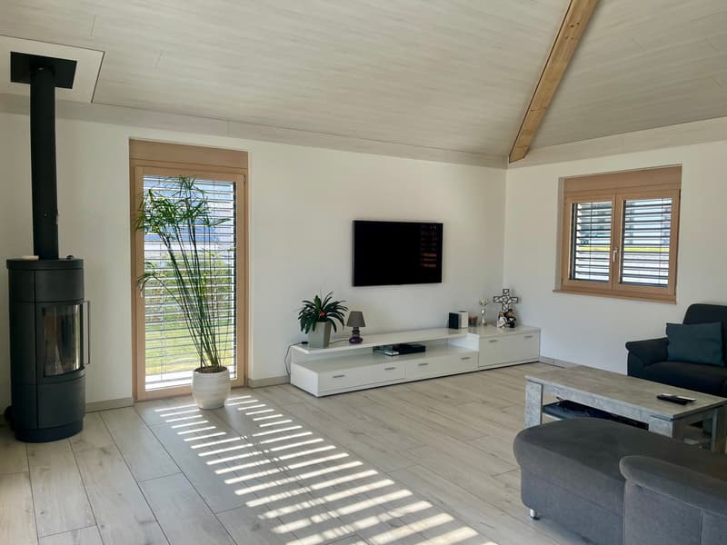 Spacious living room with hardwood floors, white walls, large windows, a fireplace, a TV mounted on the wall, a white TV stand, and a gray sofa and coffee table.