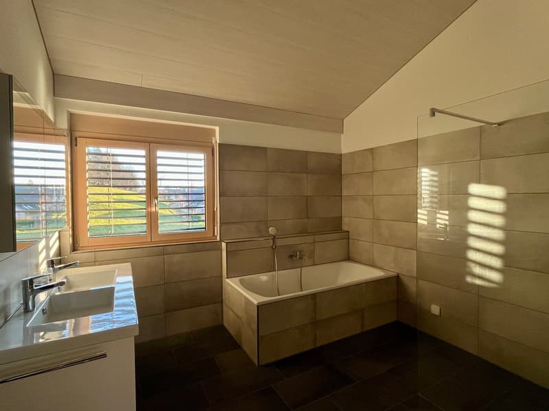 Large bathroom with tiled walls, a bathtub, and a window overlooking the outdoor scenery.