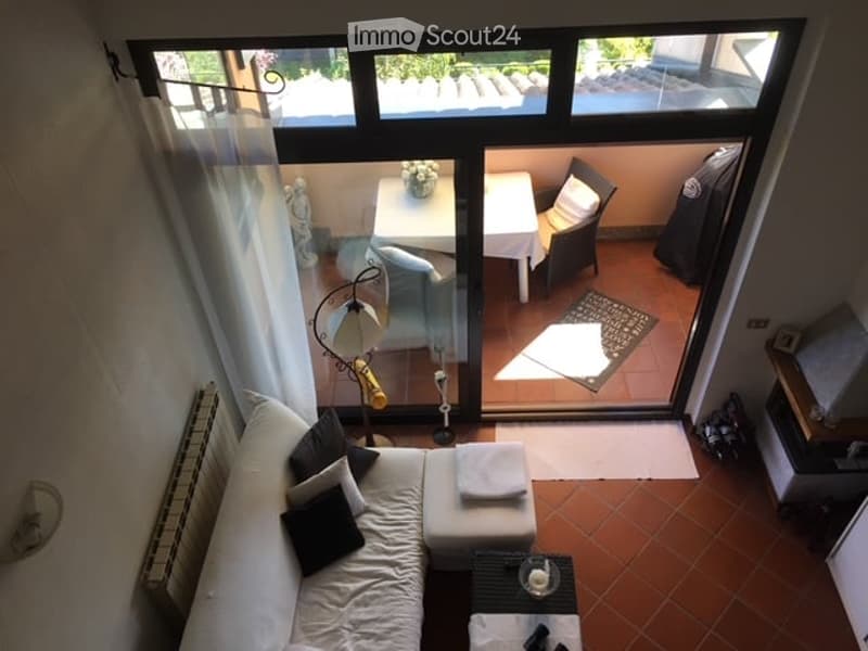 White sofa, white pillow, black pillow, white curtain, white rug, lamp, glass sliding doors, tiled floor, patio with table, chairs, plants, floor to ceiling window