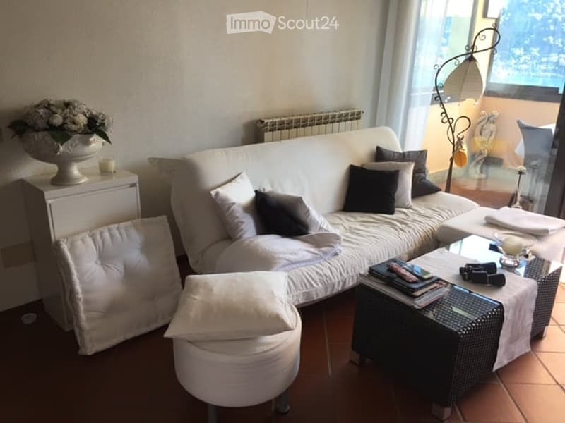 White sofa, white cushions, white cabinet, coffee table, glass vase with flowers, white floor, large window