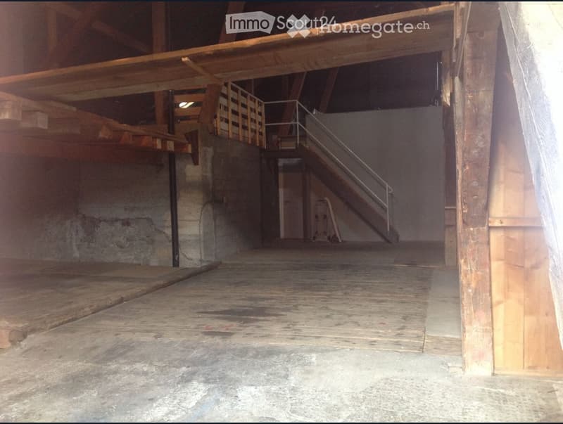 The image shows an attic space with a wooden beam structure and a wooden floor. The space appears to be dimly lit and has a rustic, unfinished appearance.