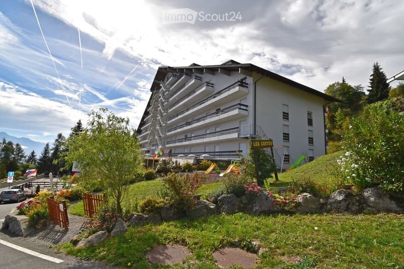 Large white building, balconies, trees, mountain in the background