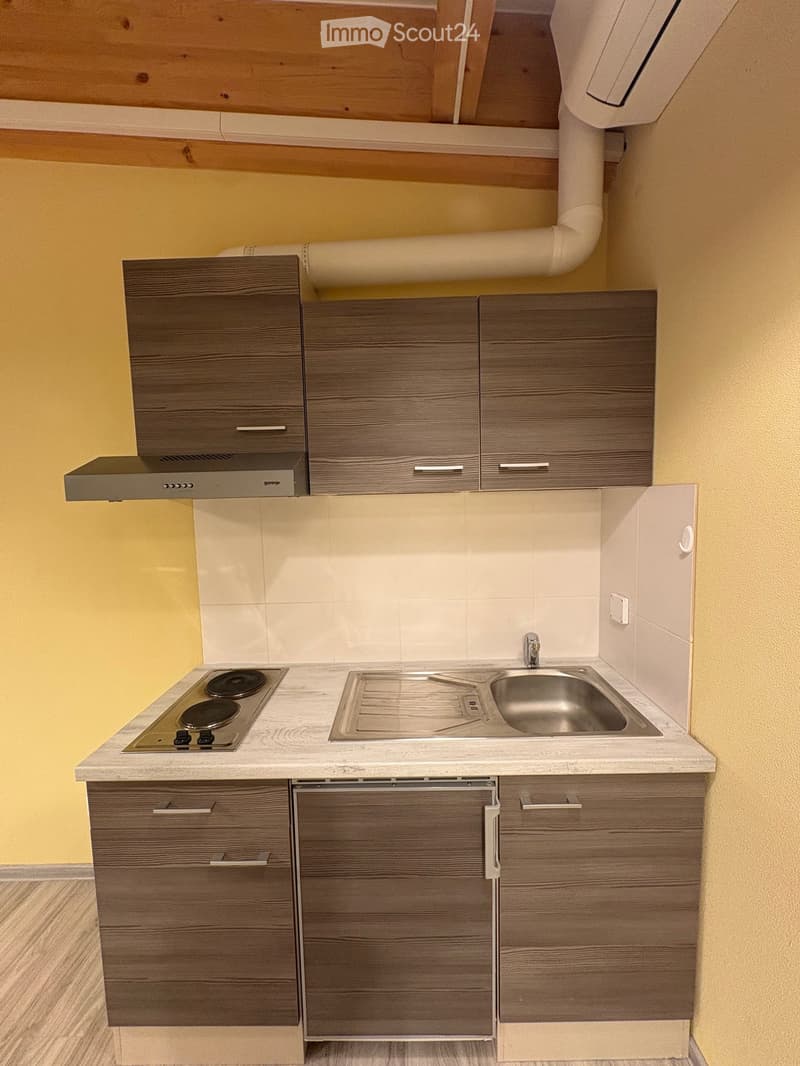 A kitchen with a stove, sink, and cabinets, gas duct, exhaust hood