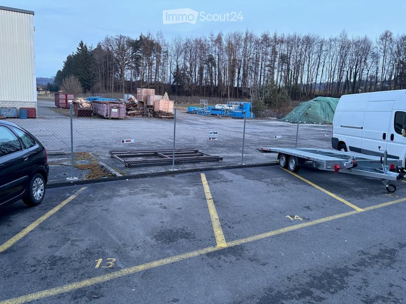Car park area with empty parking spaces, a white van, and a fence.