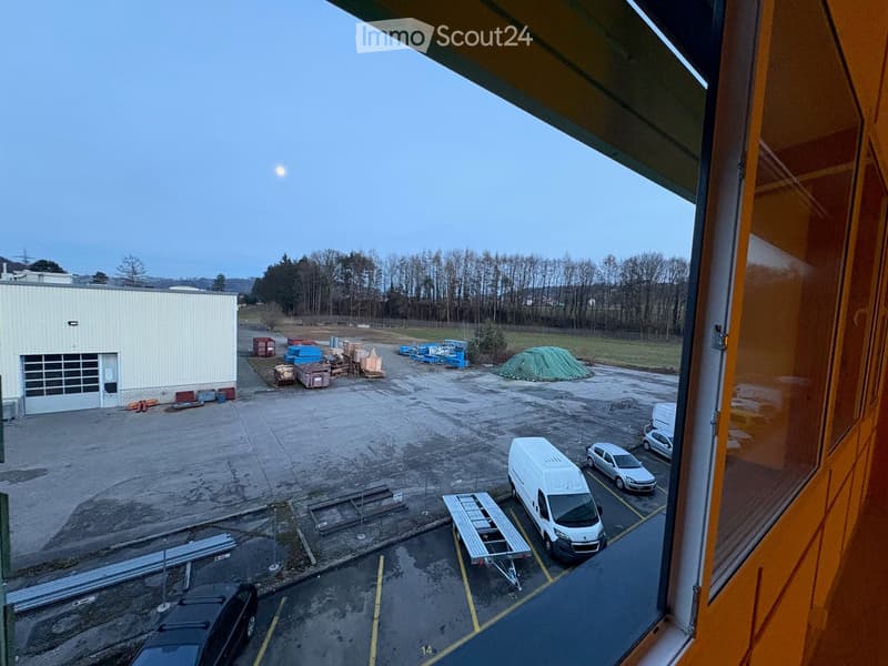 Outdoor parking area with various vehicles, building, fenced area, construction materials