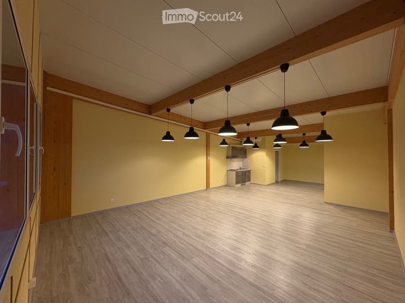 empty room, wooden floors, yellow walls, white ceiling, wooden beams, hanging lamps, kitchenette in corner