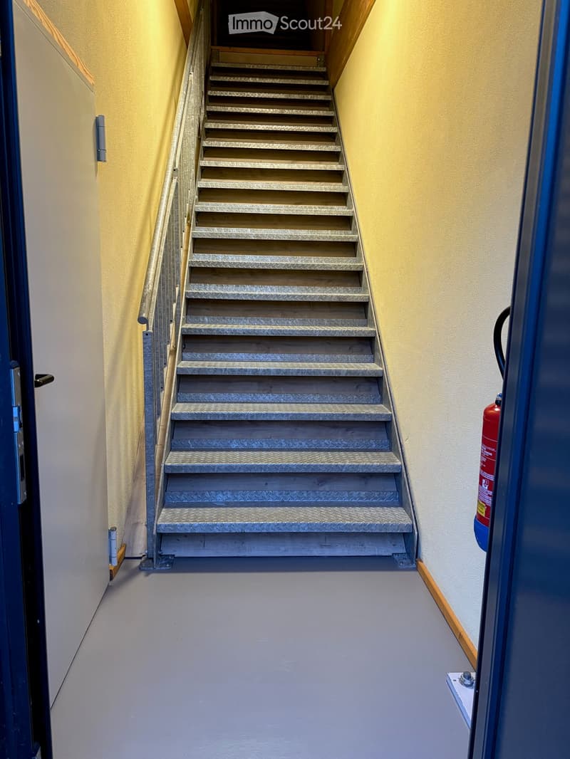Staircase with metal handrail, concrete floor, fire extinguisher on the right