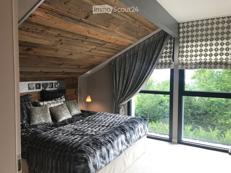 A bedroom with a large bed, wooden ceiling, pillows, and large windows offering a view of trees