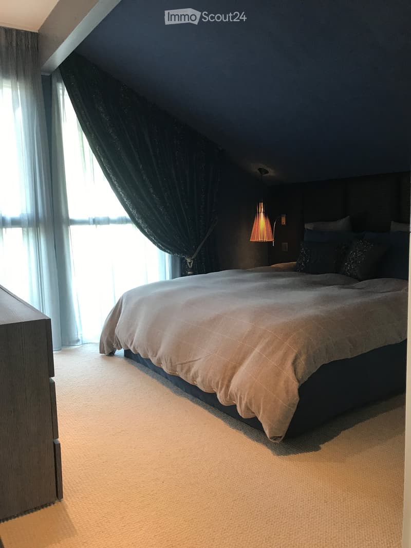 Bedroom with carpet, large bed, white curtains, dark blue ceiling, bedside lamp, wooden cabinet
