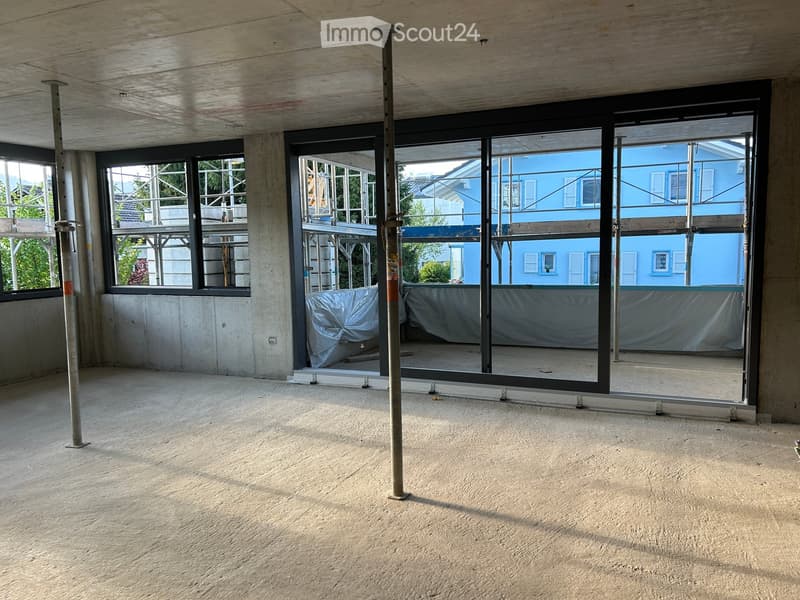 Empty room with concrete floors and walls, large windows, and metal support columns. No furniture or equipment present.