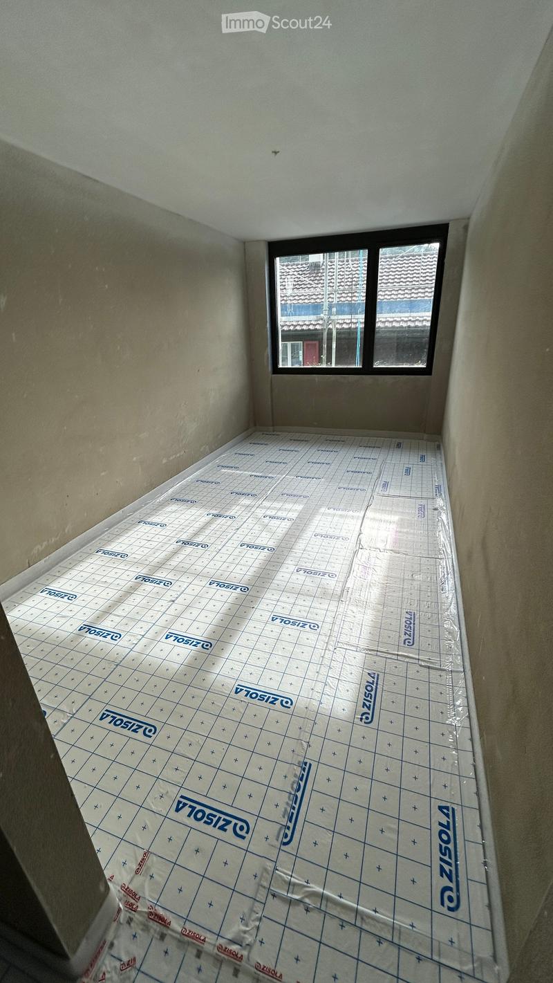 Empty room with bare walls and a window, covered with a protective floor covering material.