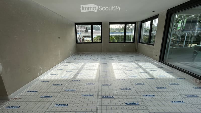 Empty room with bare walls and a tiled floor, featuring large windows and natural light.