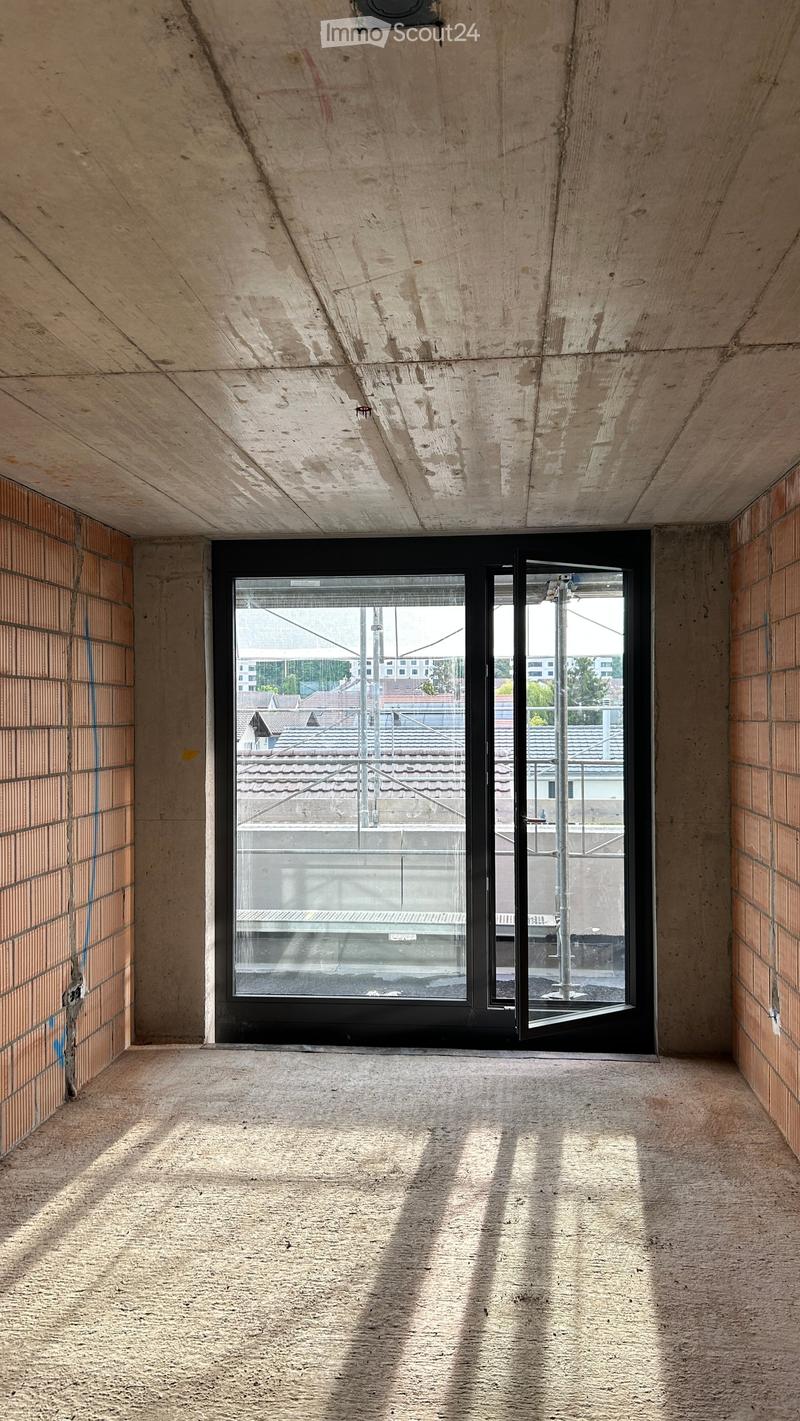 Empty room with concrete walls and floor, large window showing outdoor view, no furniture or equipment.