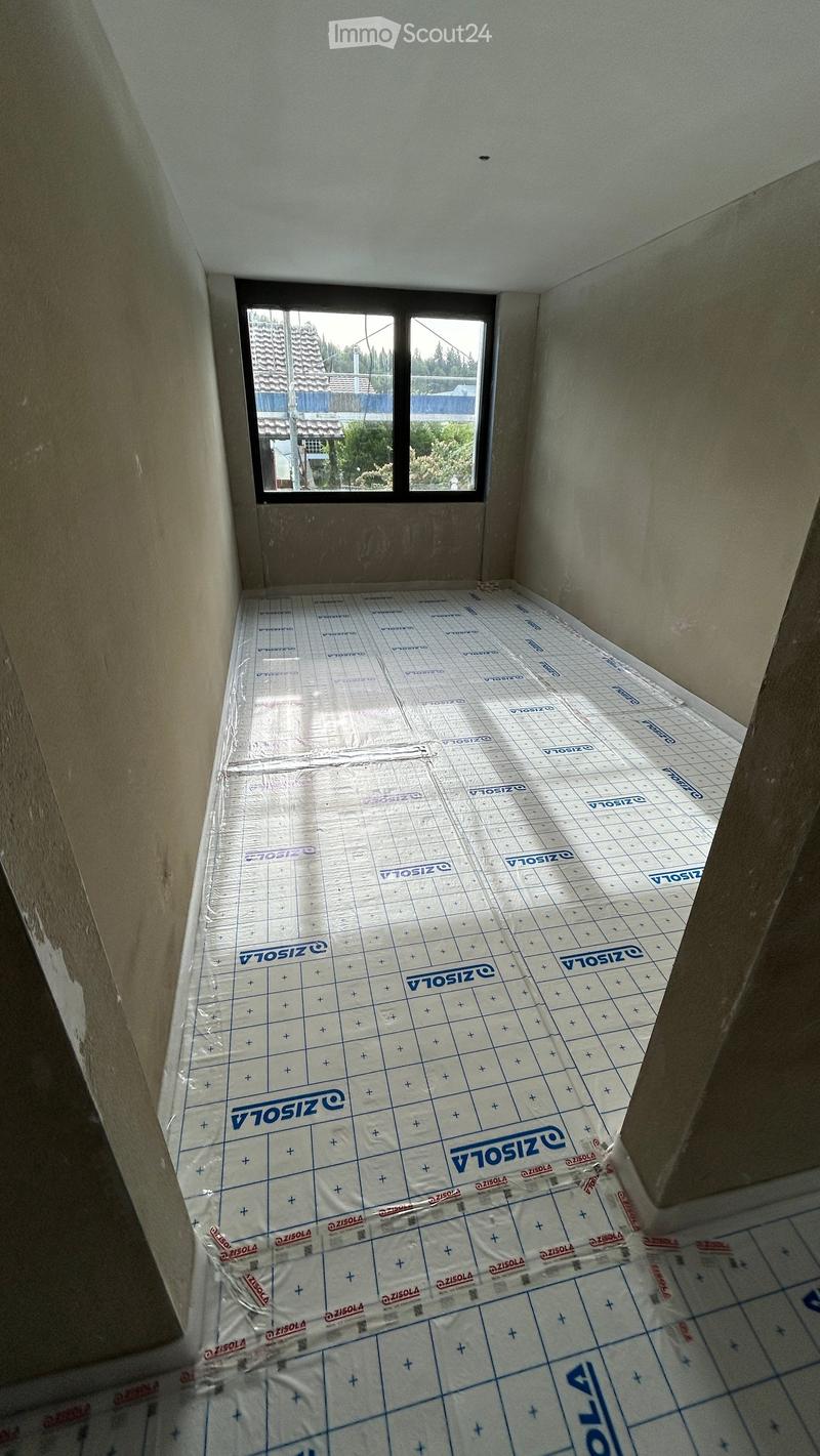 Empty room with bare walls and a plastic floor covering, featuring a window showing a view of the outside.