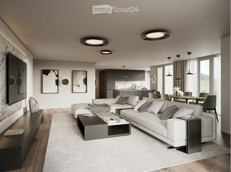 Spacious open-concept living room with modern furniture, including a large sectional sofa, coffee table, and TV. The room features large windows, providing natural light and a view. The kitchen area is visible in the background, with sleek gray cabinets a
