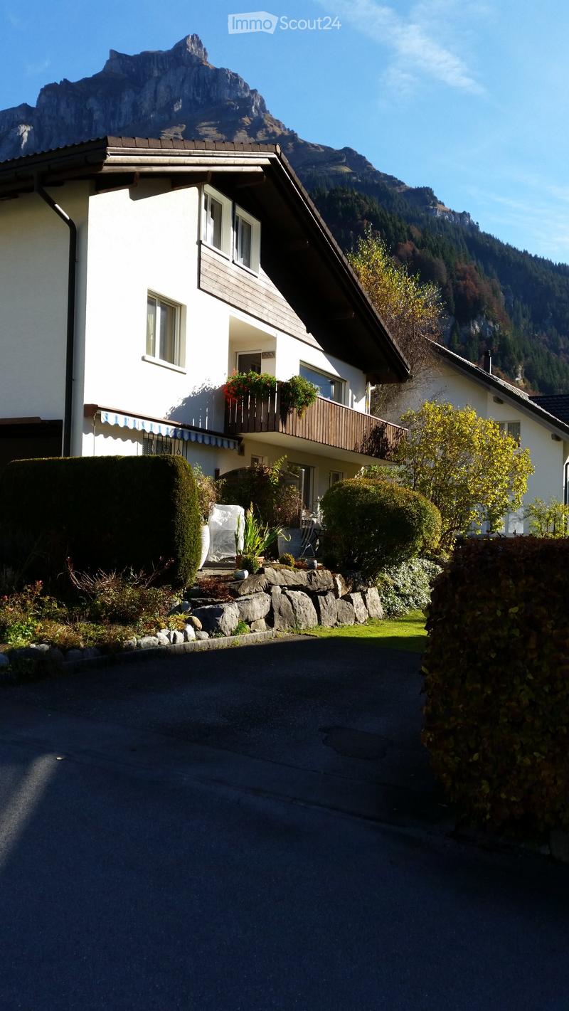 2-story white house with a balcony, surrounded by a garden and landscaping, with a mountain backdrop